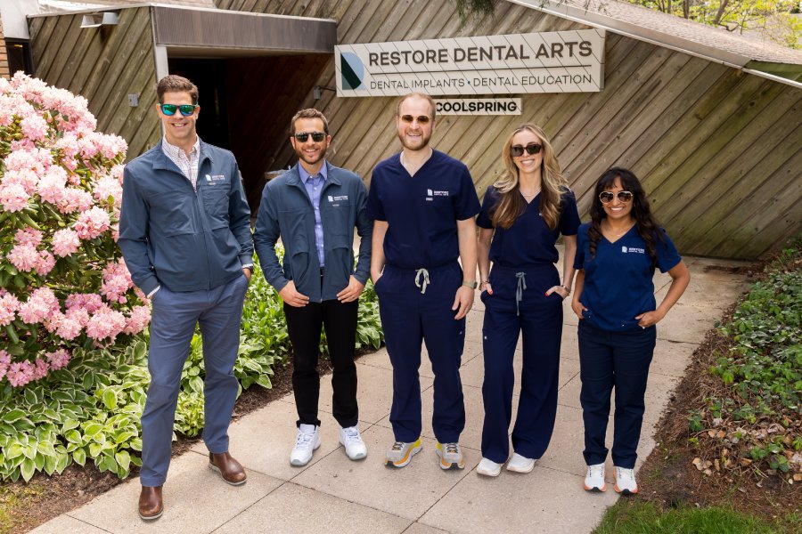Group of four smiling dental professionals posing in a modern clinic lobby.