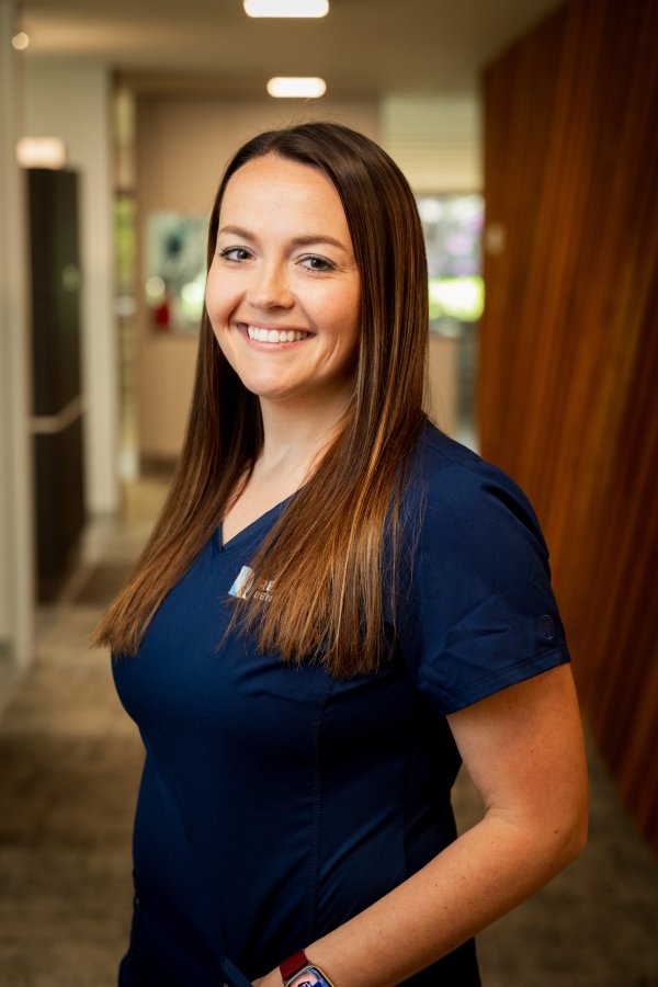 Smiling woman in navy scrubs standing in a clinic hallway, ready to help patients.