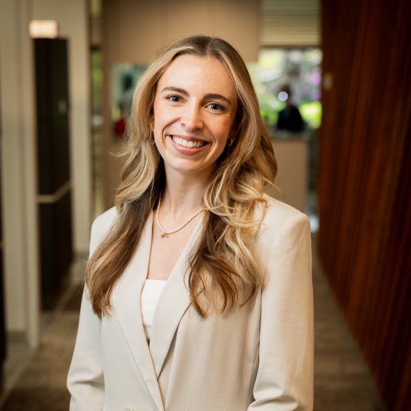 Dr Myrick | Restore Dental Arts Smiling woman with long blond hair in a cream blazer standing in a modern office hallway.