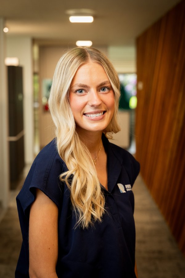 Portrait of a smiling woman with long blonde hair in a navy uniform standing in a hallway.