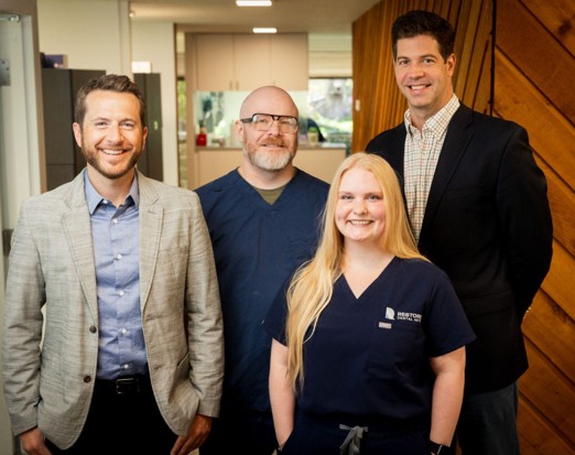 RestoreLab Group of four professionals posing for a photo in an office, with one woman in navy scrubs at center flourish, smiling.